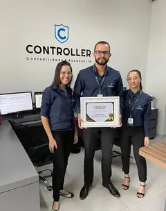 Vitor Rodrigues Dias e duas pessoas da equipe, de camisa da Controller, segurando o certificado de 2024 no escritório.